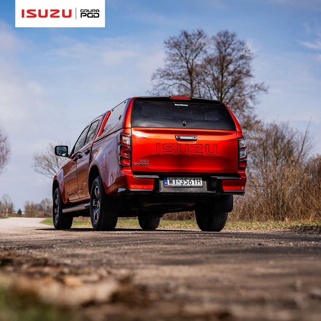Czerwone ISUZU D-MAX 2025 widziane z tyłu na wiejskiej drodze, z widoczną nazwą modelu na klapie bagażnika