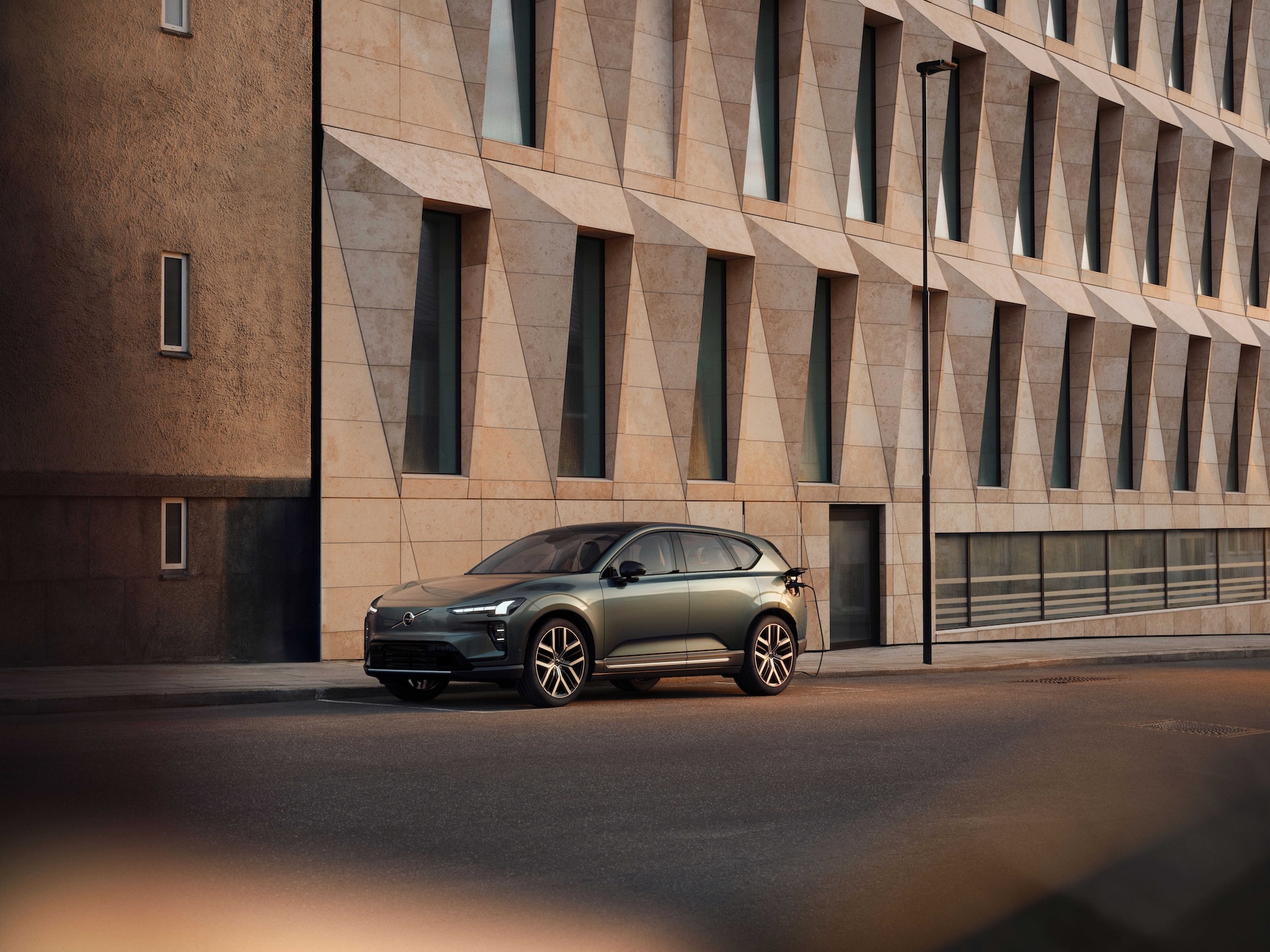Elektryczny SUV Volvo EX60 zaparkowany na miejskiej ulicy przed nowoczesnym budynkiem o geometrycznej fasadzie.