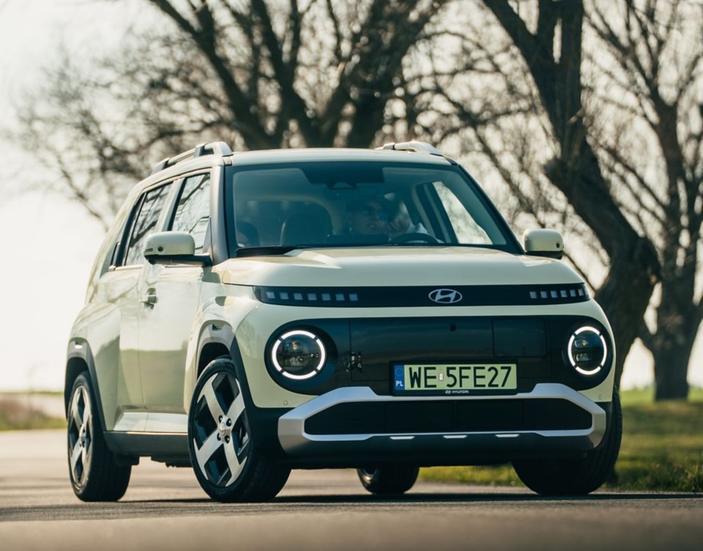 Elektryczny Hyundai INSTER w kolorze kremowym podczas jazdy po miejskiej drodze, widok na przód auta.