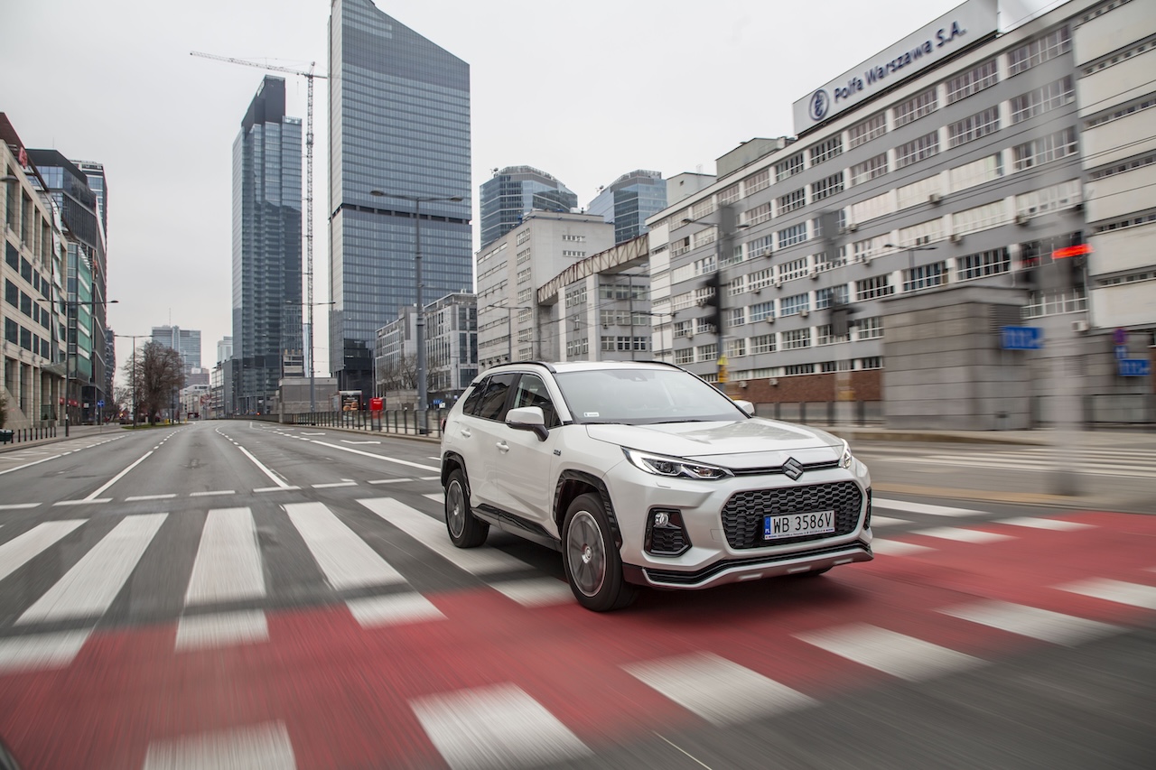 Suzuki Across w ruchu na tle miejskich wieżowców