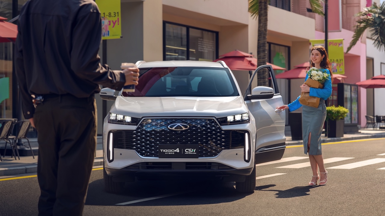 Przód białego SUV-a Chery Tiggo 4 HEV zaparkowanego na słonecznej ulicy; kobieta z kwiatami otwiera drzwi pasażera.