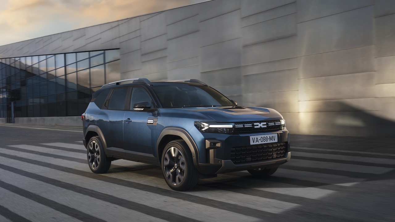 Dacia Bigster w kolorze Indigo Blue jadąca wzdłuż nowoczesnego budynku z przeszkleniami