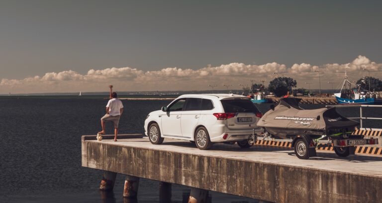 SUV Mitsubishi Outlander z przyczepą na łódź, w porcie na tle morza