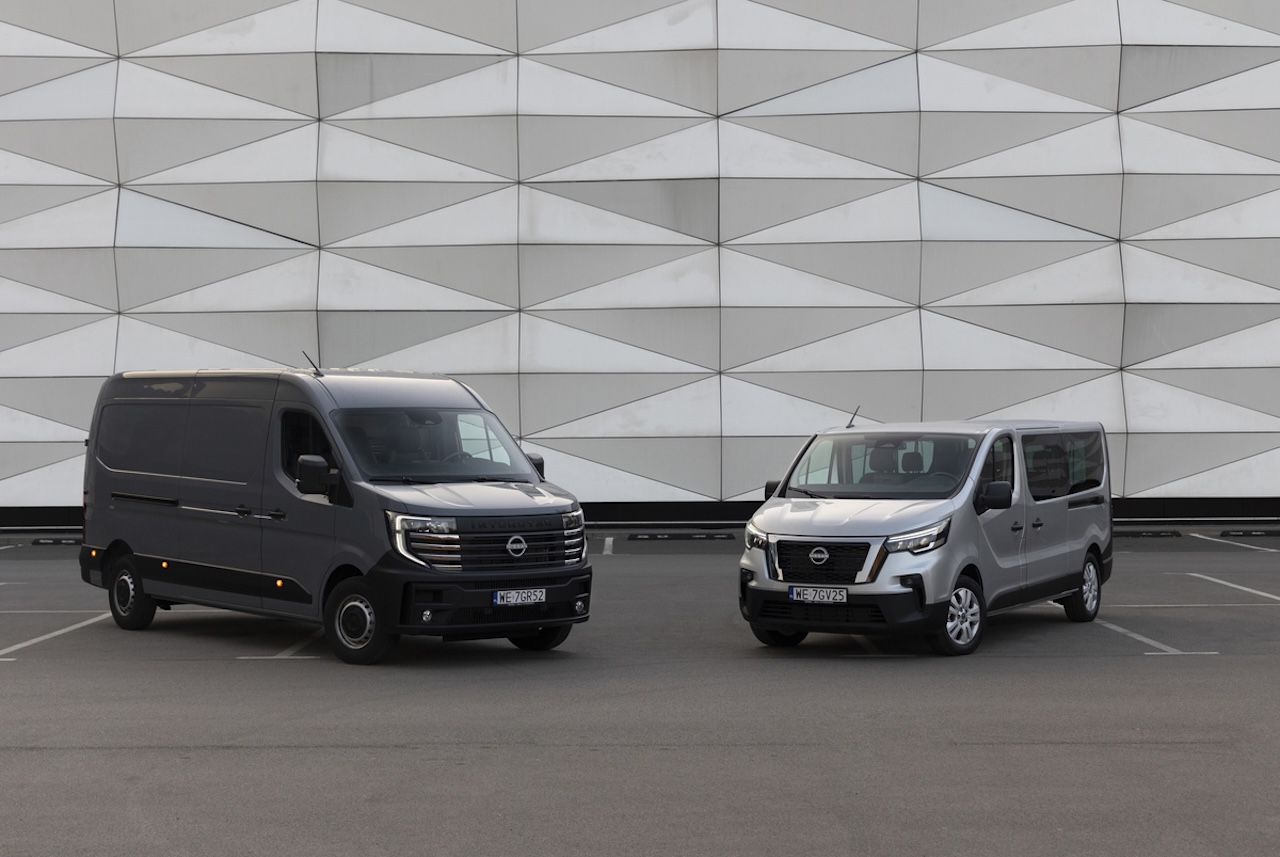 Dwa samochody dostawcze Nissan – szary furgon Interstar oraz srebrny bus Primastar – zaparkowane obok siebie przed białą elewacją o trójkątnym, geometrycznym wzorze.