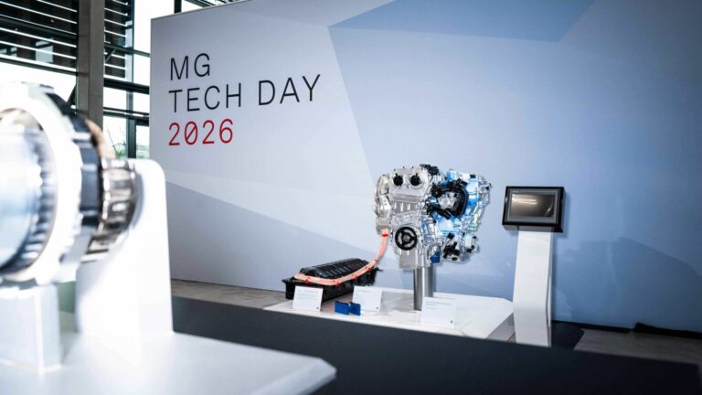 Stanowisko ekspozycyjne MG Tech Day 2026 z dużym napisem na białej ścianie oraz srebrnym silnikiem spalinowym i ekranem kontrolnym na białym postumencie.