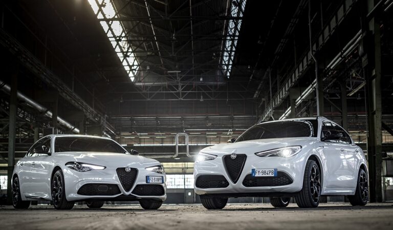 Alfa Romeo Giulia i Stelvio z silnikiem 2.0 benzyna – widok z przodu na oba białe modele w industrialnej hali.