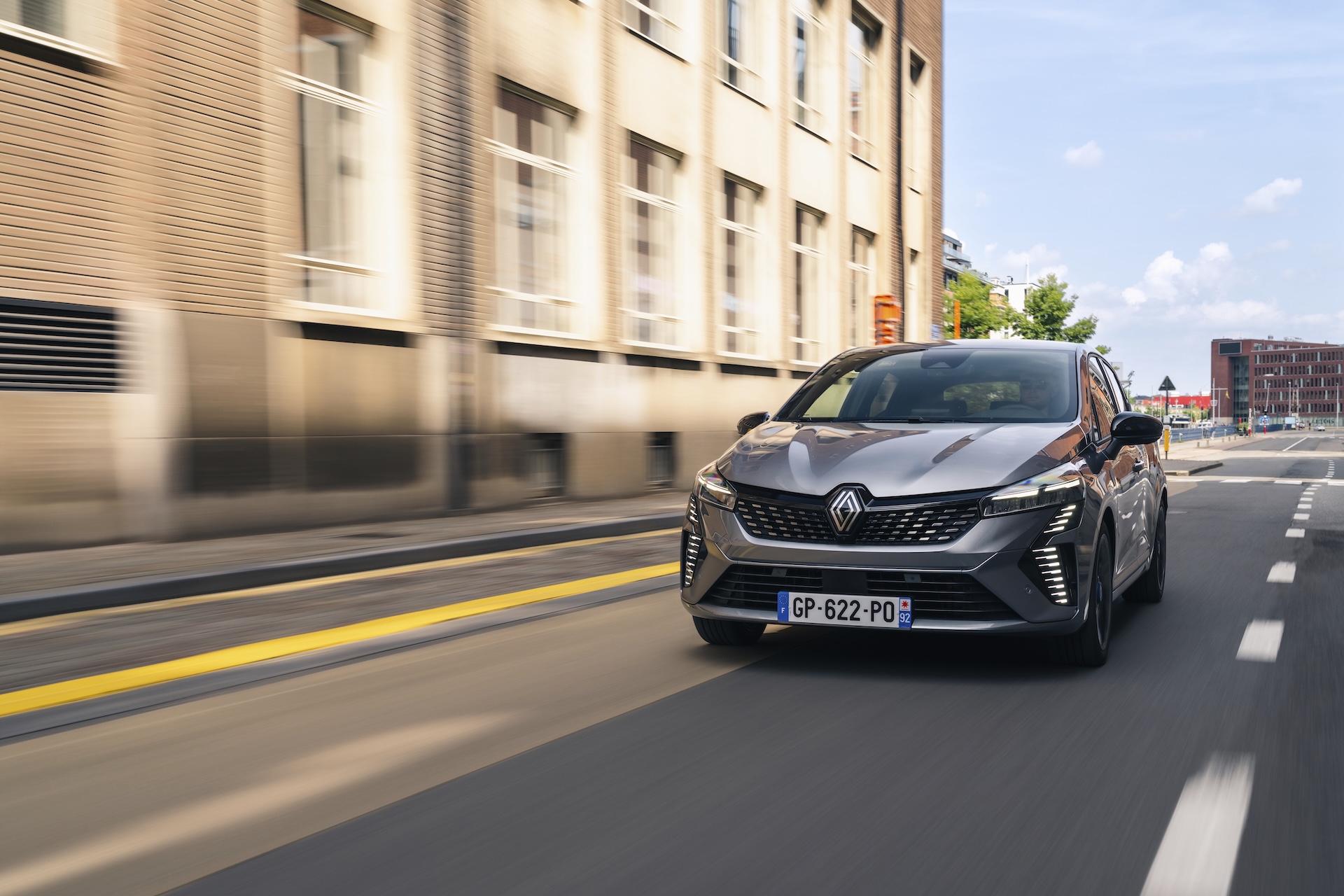 Srebrny Renault Clio E-Tech jadący ulicą w centrum miasta.