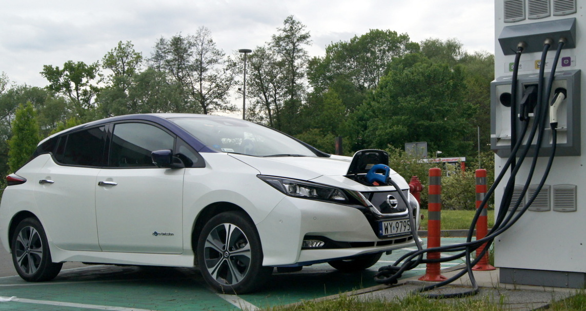 białe auto elektryczne Nissan Leaf na stacji ładowania, czy opłaca się kupić używany samochód elektryczny