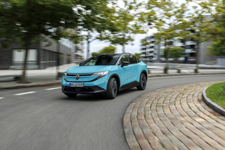 Nowy Nissan LEAF w dynamicznym ruchu na miejskiej drodze, ukazujący płynną linię nadwozia typu crossover.