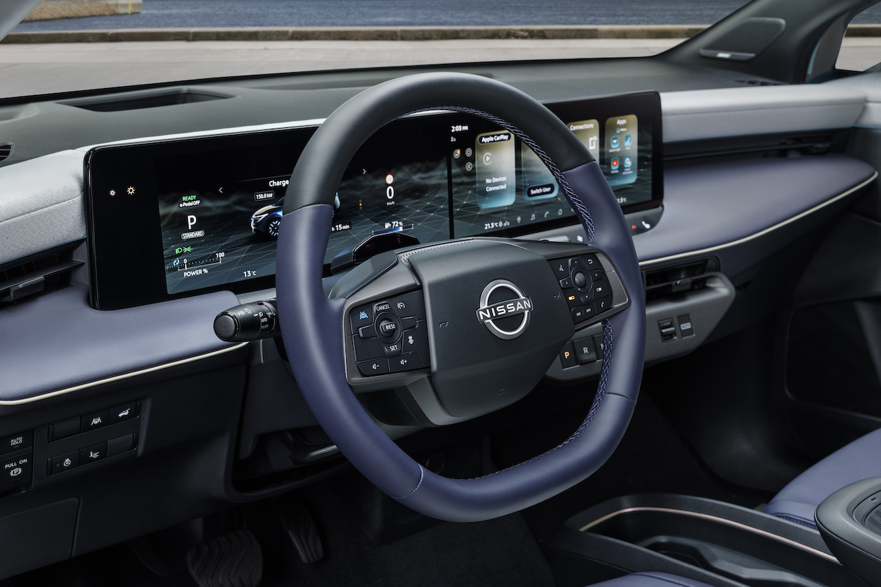 Zbliżenie na kierownicę z logo Nissana oraz nowoczesny, szeroki panel z dwoma wyświetlaczami systemu NissanConnect.
