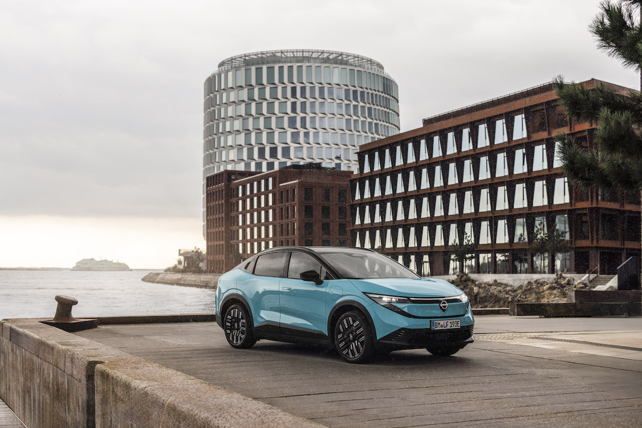 Turkusowy Nissan LEAF zaparkowany na betonowym nabrzeżu portowym na tle nowoczesnej, miejskiej architektury.