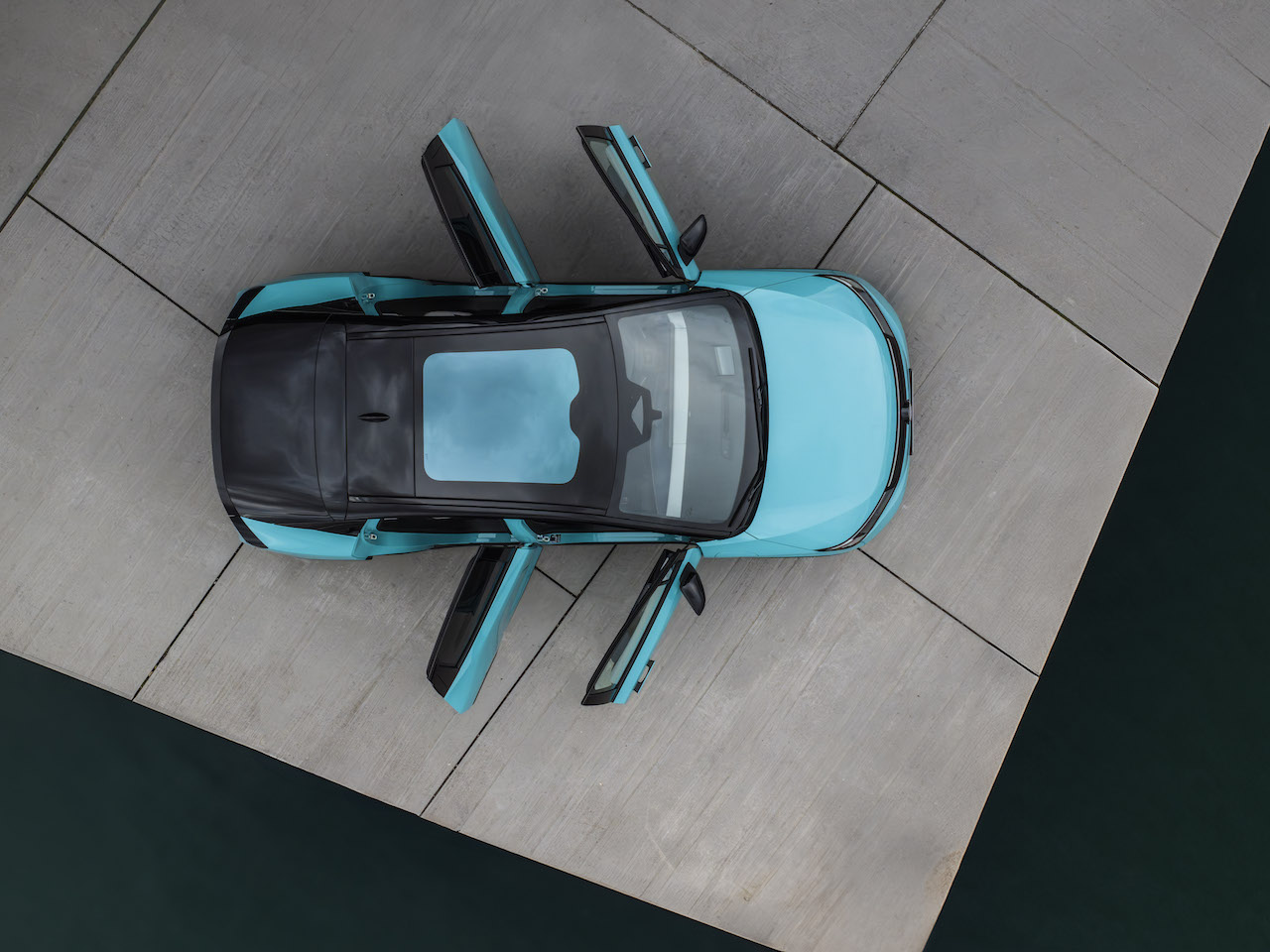 Zdjęcie z lotu ptaka na turkusowego Nissana LEAF z otwartymi wszystkimi drzwiami, prezentujące czarny, panoramiczny dach.