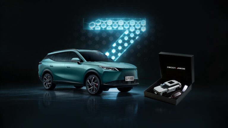 Nowoczesny SUV OMODA 7 w kolorze turkusowym na ciemnym tle z podświetloną cyfrą 7 w formie plastra miodu; obok czarne pudełko z modelem kolekcjonerskim i brelokiem OMODA JAECOO.