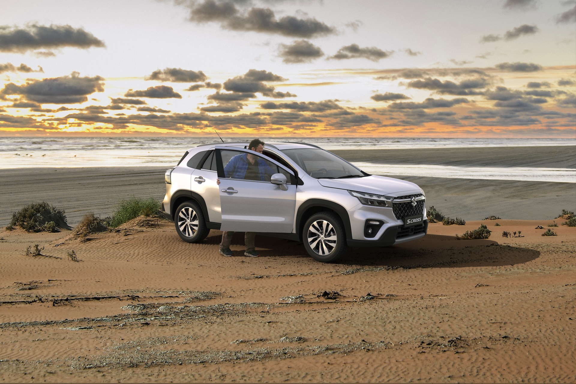 Suzuki S-Cross zaparkowany na plaży podczas zachodu słońca, mężczyzna wychodzi z samochodu.