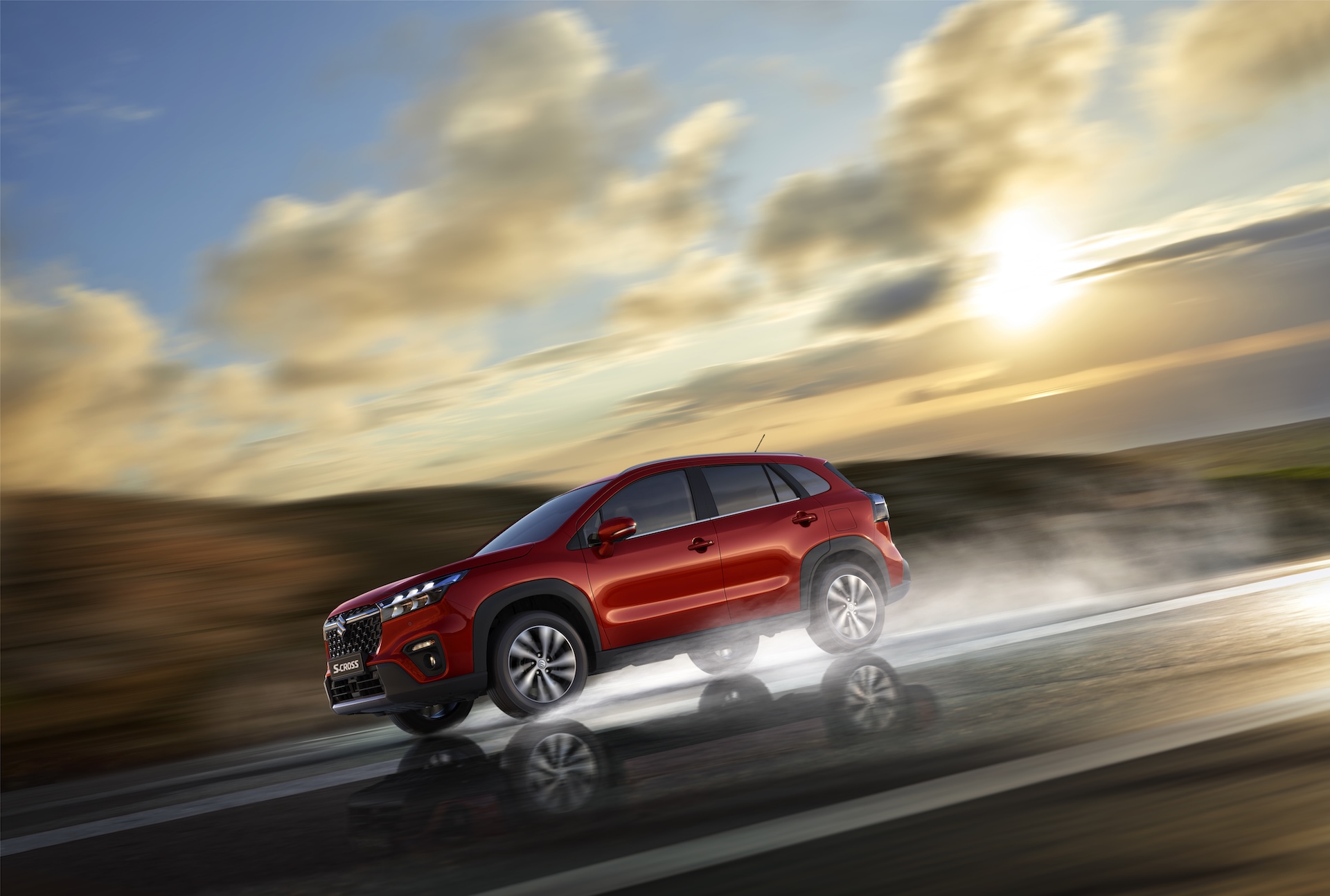 Czerwony Suzuki S-Cross w ruchu na mokrej nawierzchni, dynamiczne ujęcie przy zachodzącym słońcu.
