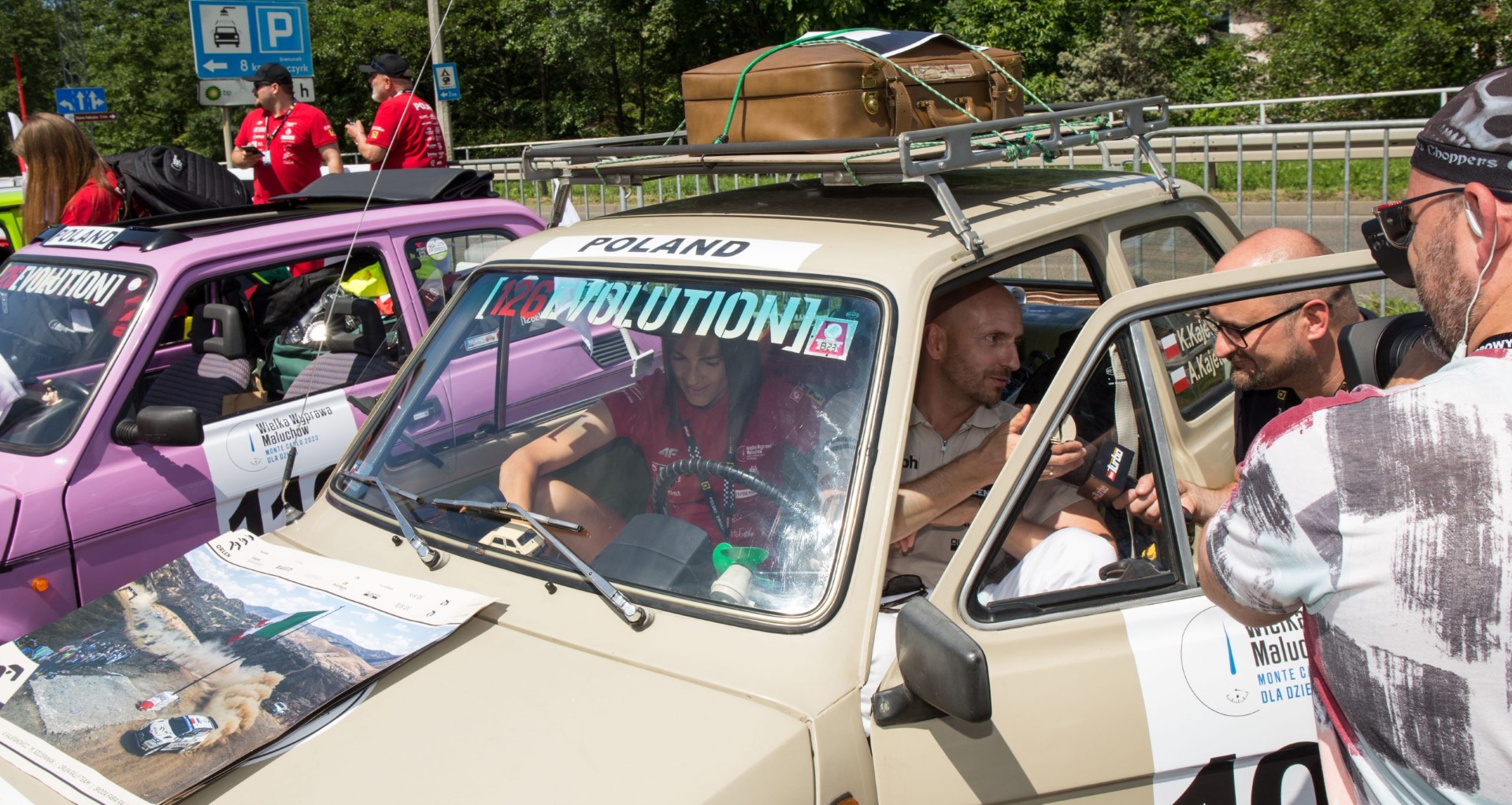 Kajetan Kajetanowicz Kajto z żoną w samochodzie Fiat 126p, na bagażniku dachowym oldskulowa walizka ze skaju start rajdu w Bielsku-Białej #jedziemypomilion