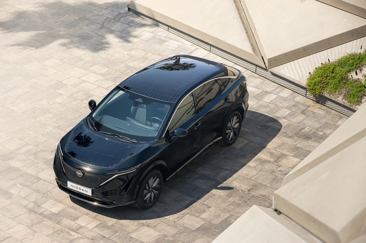 Czarny elektryczny SUV Nissan ARIYA widziany z góry, zaparkowany na jasnym placu z kamiennych płyt obok nowoczesnej betonowej architektury.