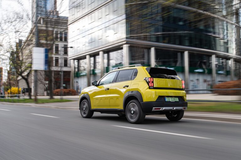 Fiat Grande Panda Electric w ruchu na tle nowoczesnej zabudowy.
