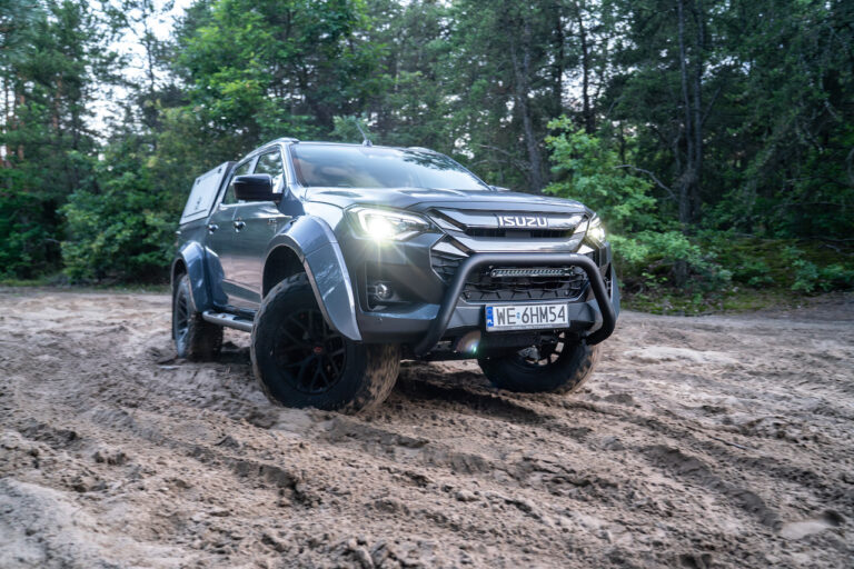 Szary ISUZU D-Max Arctic Truck 2025 przedzierający się przez piaszczysty teren w lesie.