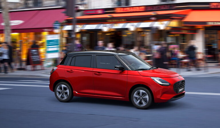 Czerwony Suzuki Swift przejeżdżający obok kawiarni w ruchliwym centrum miasta